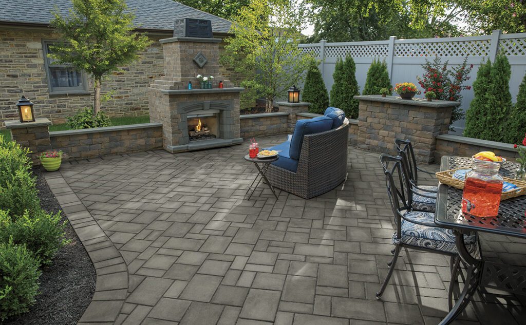 Photo shows a paver patio with an outdoor fire place, table, and patio chairs.