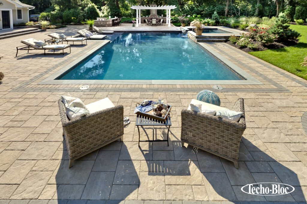 Photo shows a paver pool patio, chairs, lounges and a pergola