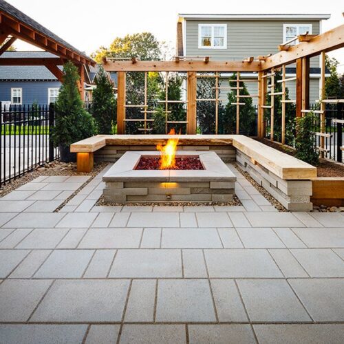 Paver patio with a fire pit, seating, and arbor behind a house